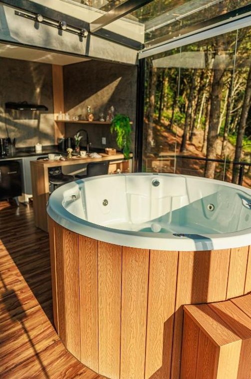 Ofurô de madeira da Cabana Cristallo com vista para a mata através das paredes de vidro