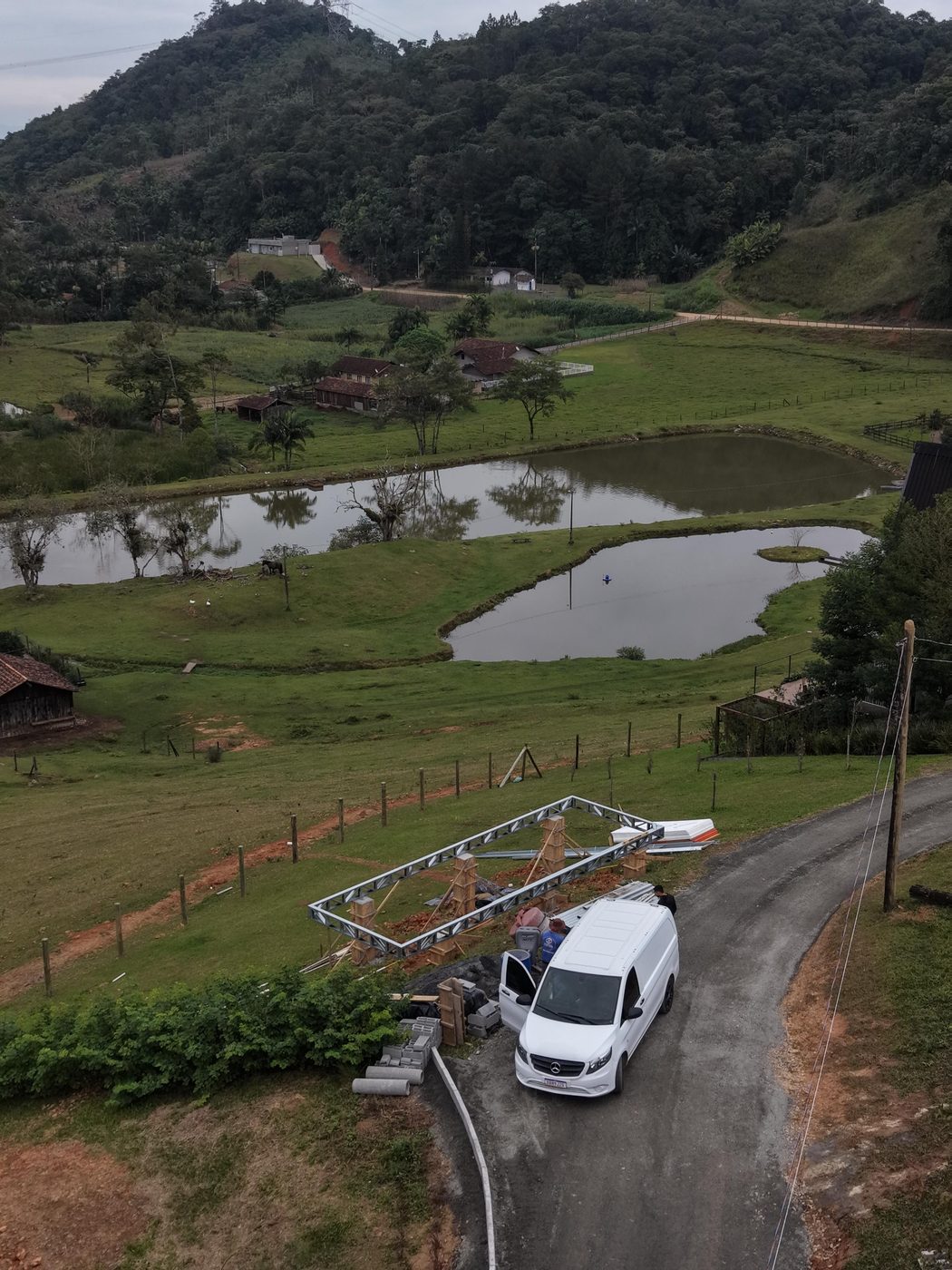Vista aérea da obra da Cabana Oásis: estrutura metálica sobre pilares de concreto, com os lagos e o vale de Pomerode ao fundo