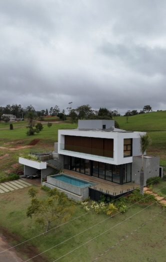 Casa de Campo em Steel Frame construída pela Construsa: fachada branca de dois volumes com brise de madeira, piscina com borda infinita e telhado com placas solares